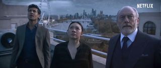 three well-dressed people stare up at the sky on a rooftop