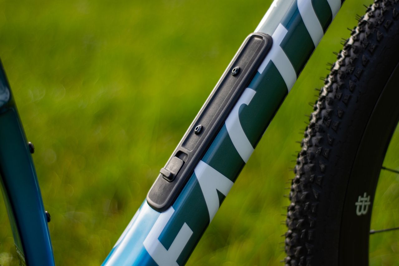 A blue Factor Sarana gravel bike in a grassy field with a hedge in the background
