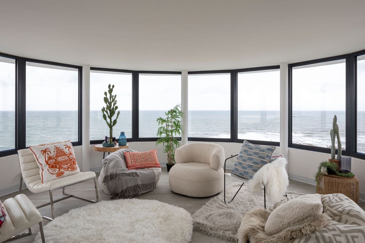 The living room again overlooks the sea with a curved room and three sofas inside the brightly lit room