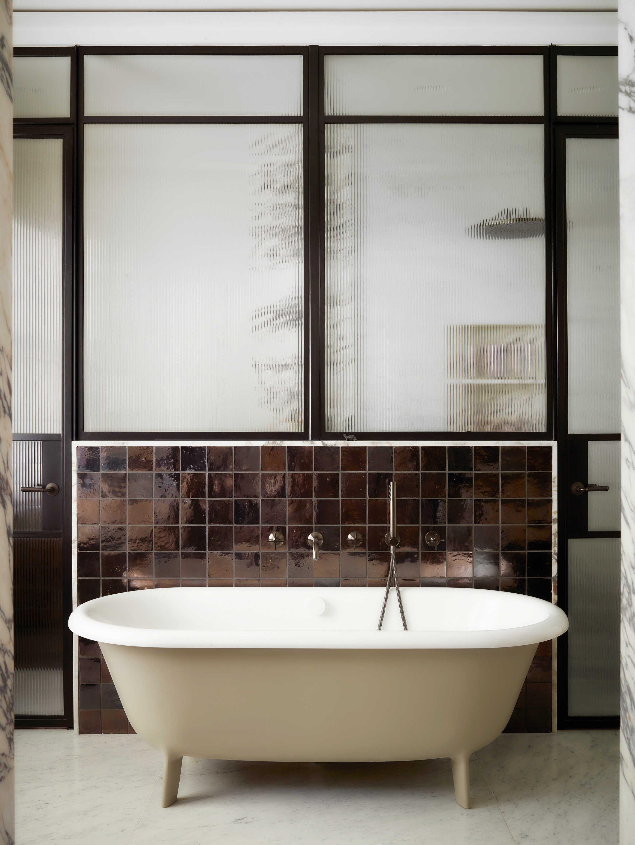 Beige freestanding bath in front of a screened wall with dark brown square zellige tiles