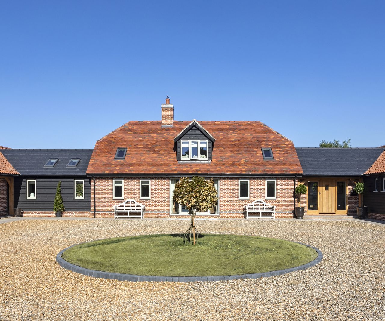 Front view of a red brick barn-style home with a large circular gravel driveway