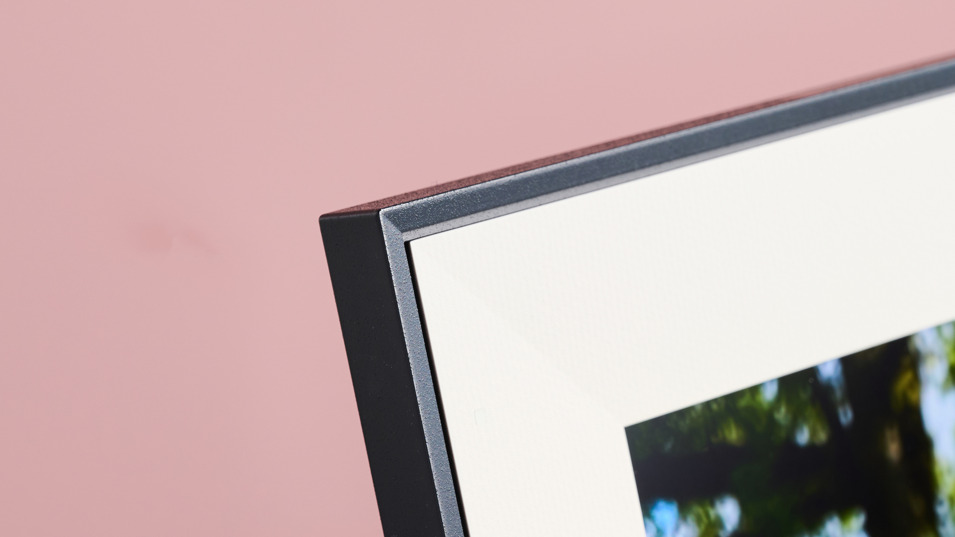 A closeup of the corner of the Aura Aspen showing its paper-like mount, in front of a pink background.