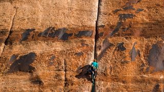 A woman lead-climbing a sandstone crack sets a route in southern Utah