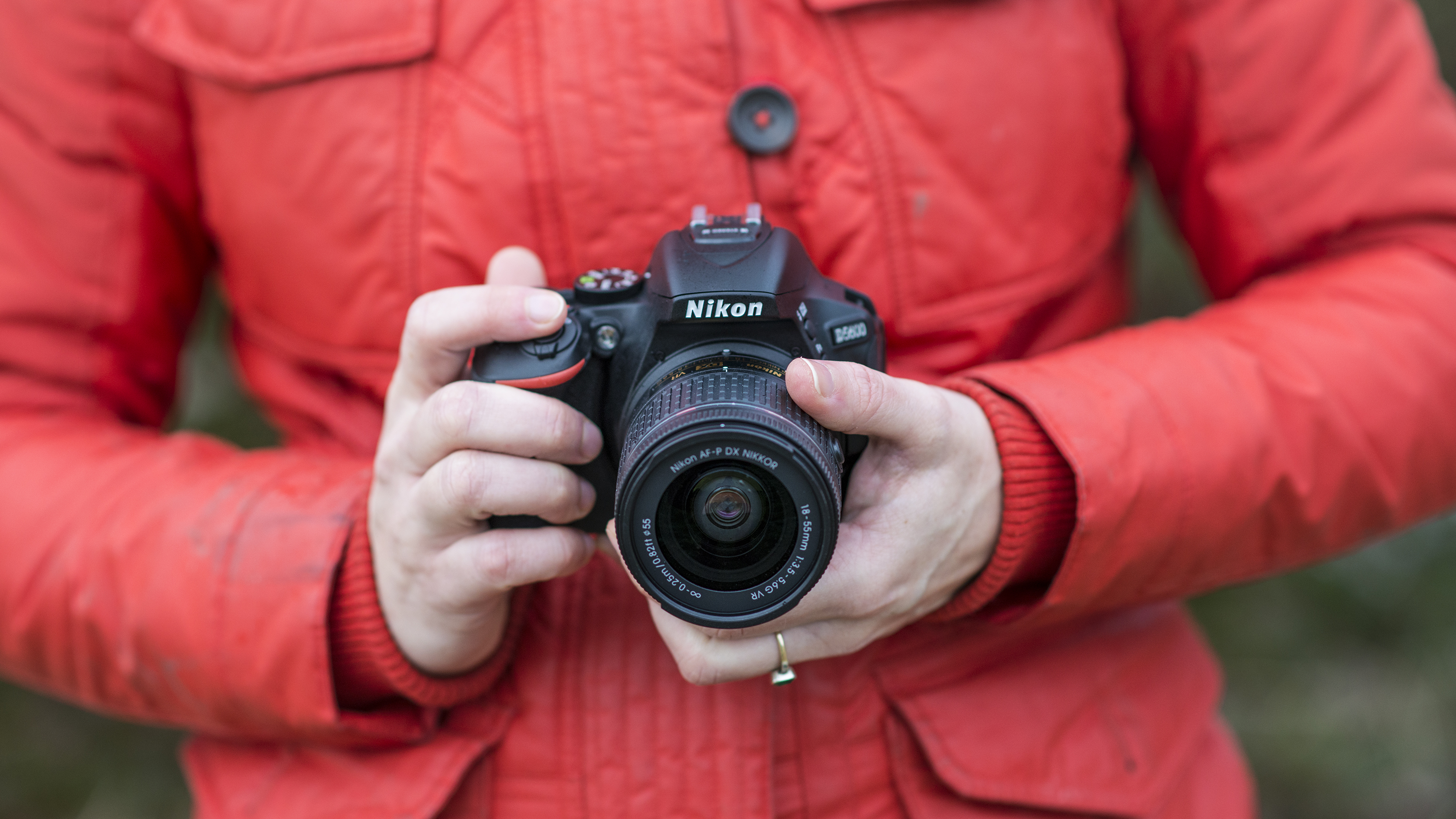 best DSLR camera Nikon D5600 being held by a person in a red jacket