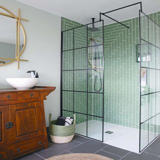 bathroom with grey floor tiles, walk in shower with green tiles, white basin and wooden bathroom drawers