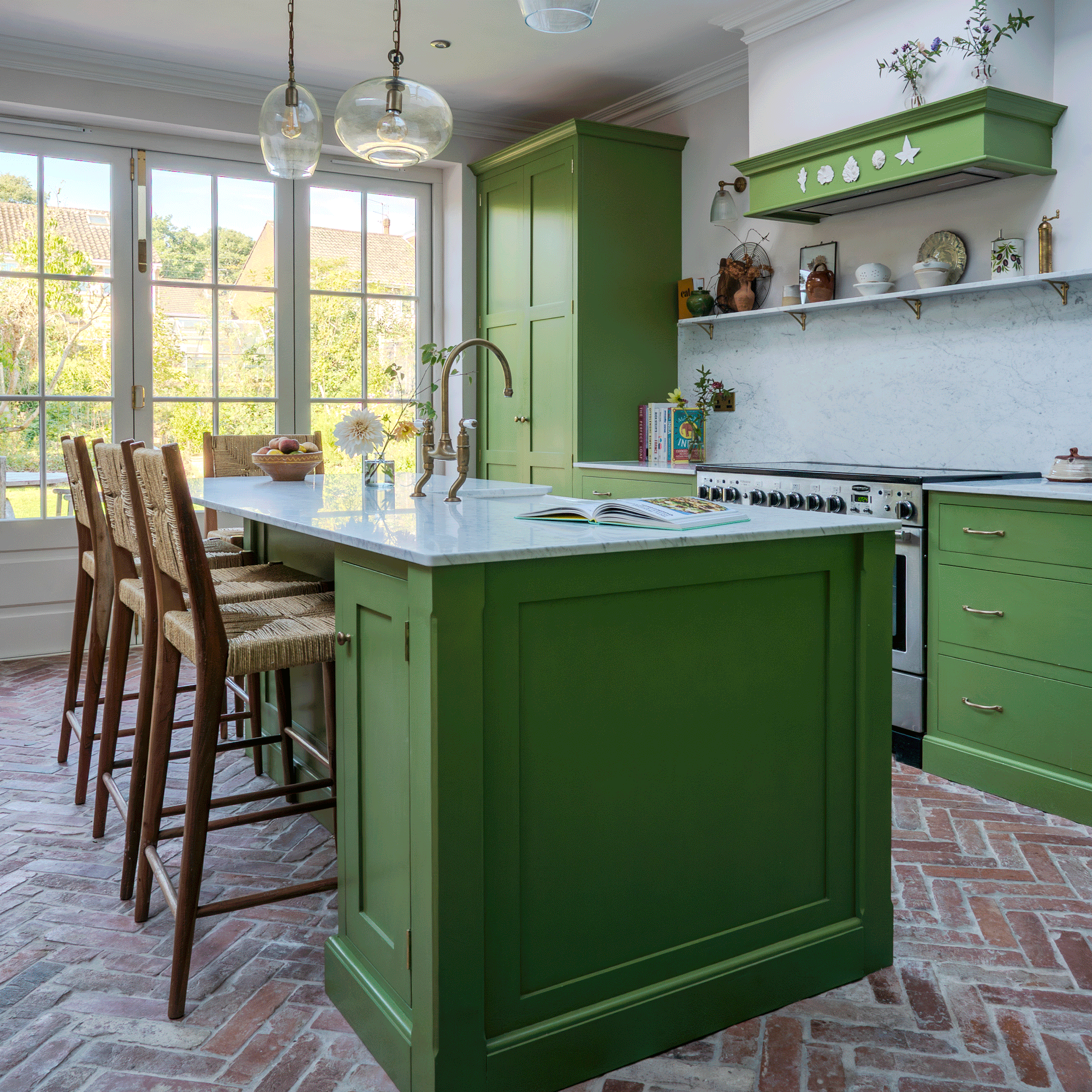 a green Shaker kitchen with herringbone flooring and patio doors a large kitchen island with four bar stools and a range cooker