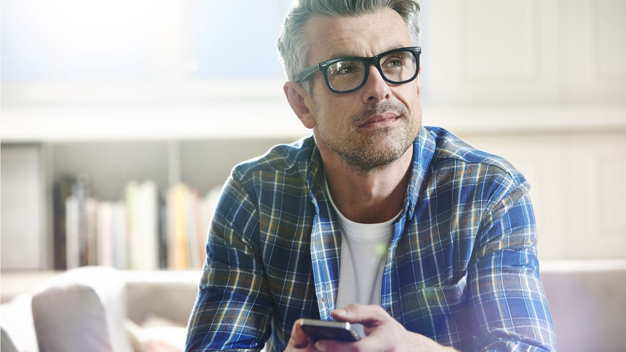 An older man in an office holds a cup of coffee and looks off in the distance as if thinking.