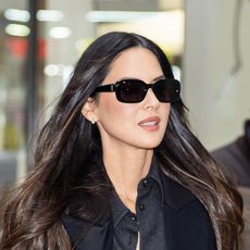 Olivia Munn wearing a black satin coat, black button down, and leather skirt