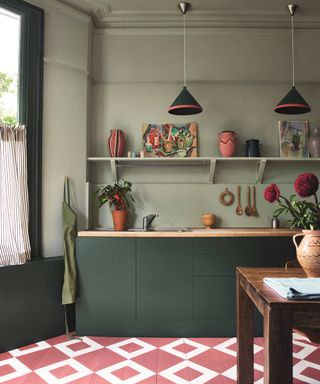 green painted kitchen with dark green units, open shelving, dark pink and white geometric tiled floor and striped cafe curtain at large window