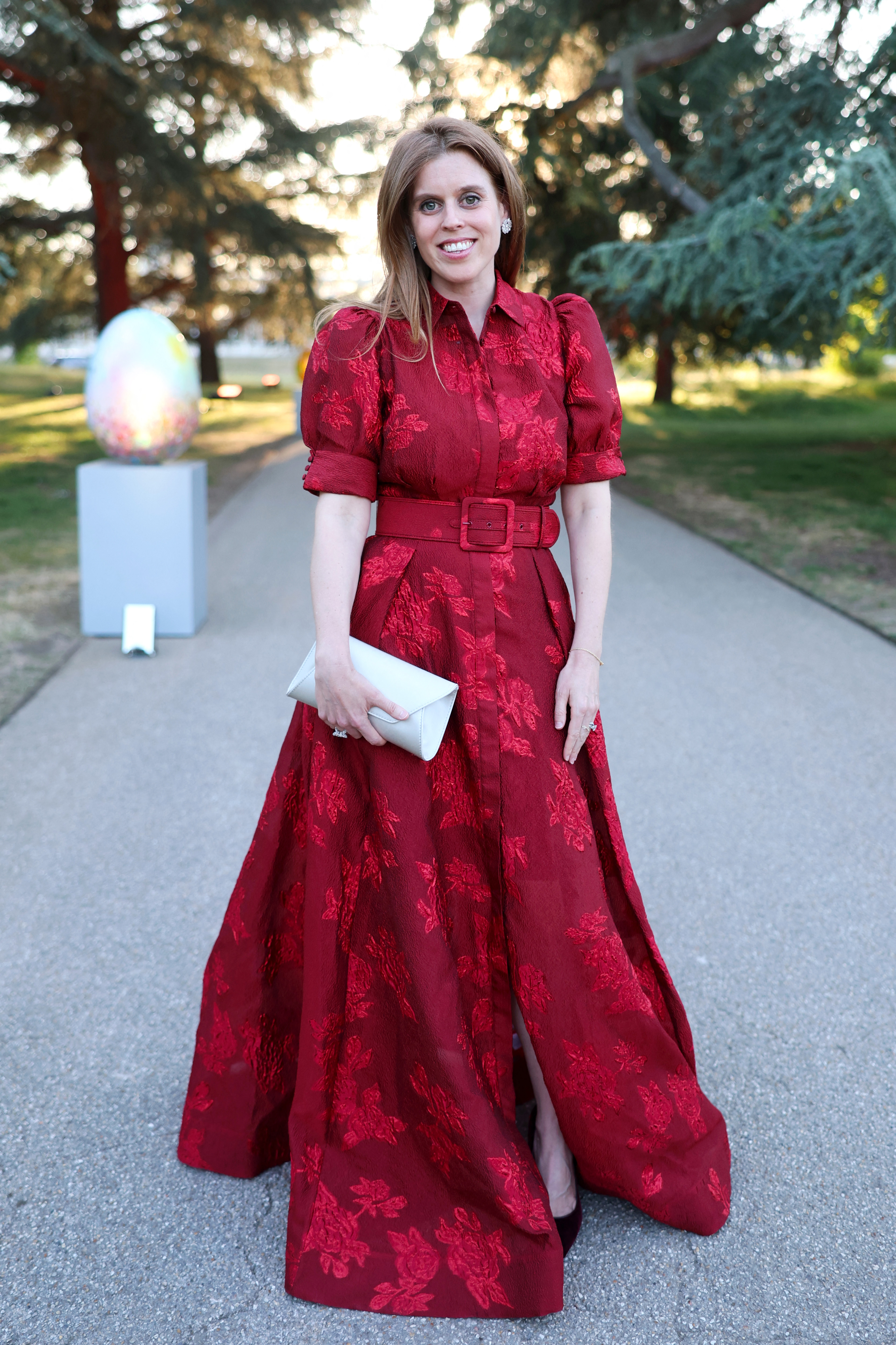 Princess Beatrice in a red gown smiling outside in front of trees