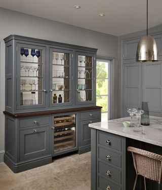 Kitchen with grey painted dresser and island, stone floor and grey walls