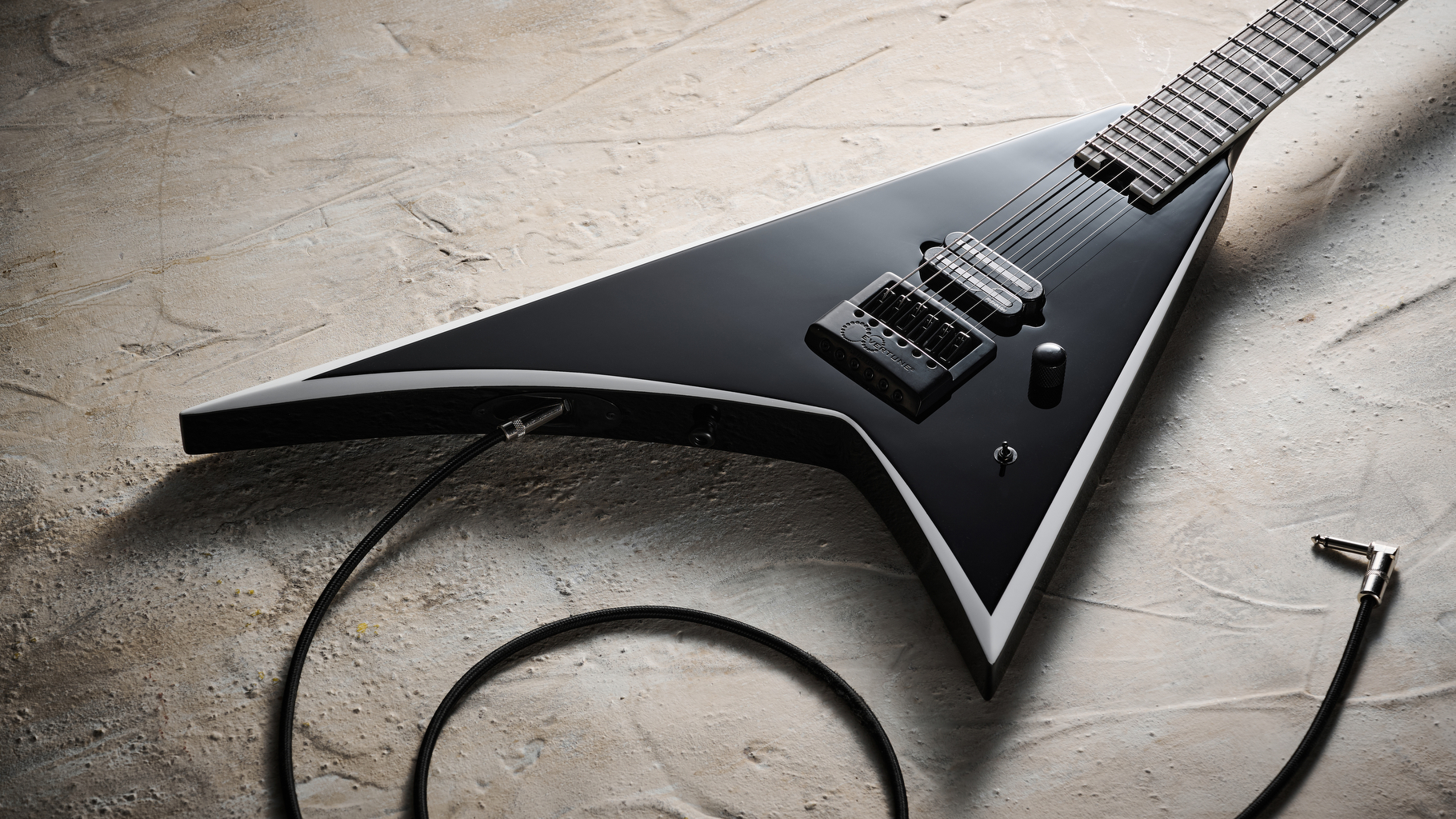 A Jackson Pro Plus Series Signature Christian Andreu Rhoads RR24 EVTN6 lying on a white, distressed floor with a guitar cable trailed nearby