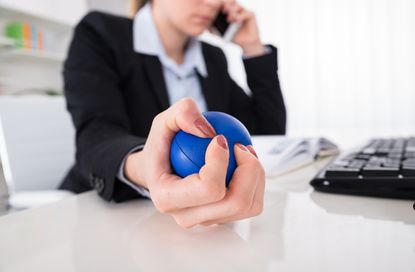 Young Businesswoman Pressing Stressball While Talking On Mobile Phone At Desk