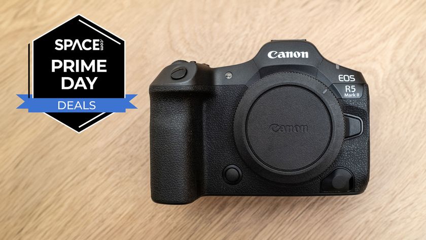 A Canon EOS R5 Mark II with the sensor cap screwed on on a wooden table with a black Space.com Prime Day deals badge in the upper left corner.