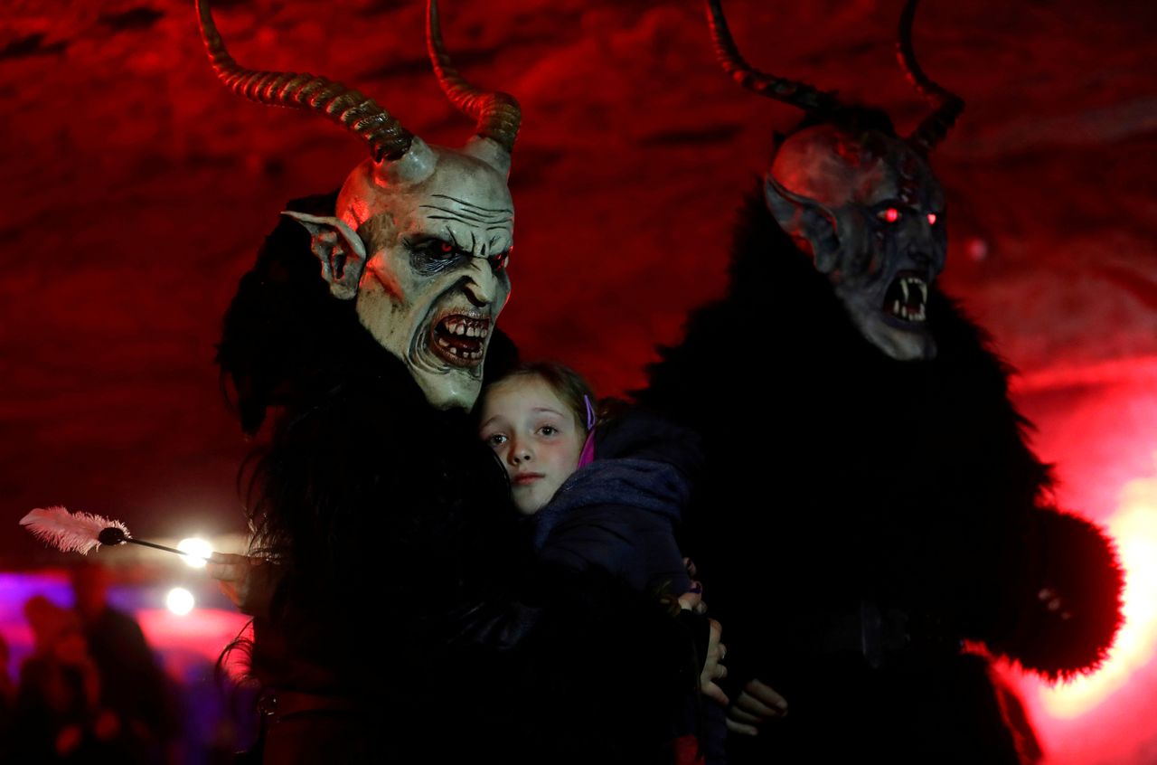 A man dressed as a devil embraces a child.