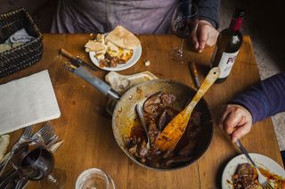 Cooked pork in a pan on a table with a bottle of red wine