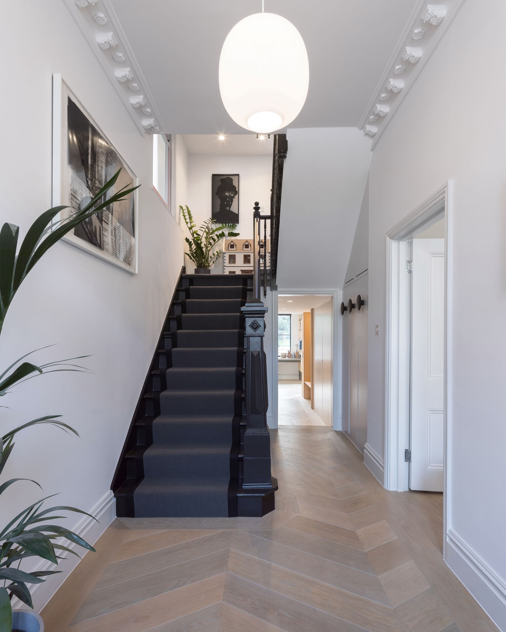 A darkly painted staircase in a hallway with herringbone patterned wooden flooring