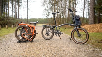 An orange Brompton covered in mud on a light gravel track