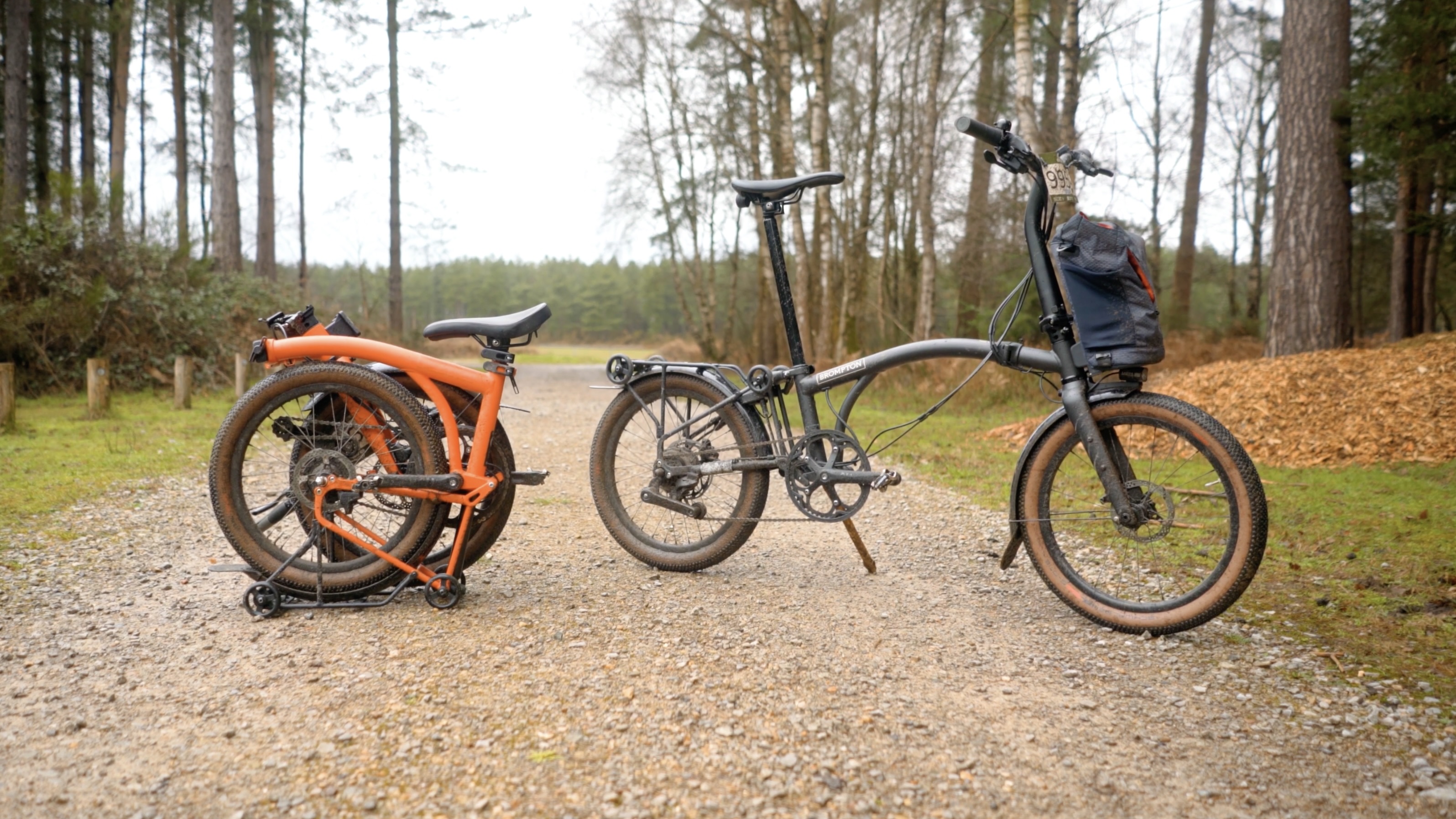 An orange Brompton covered in mud on a light gravel track