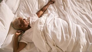 A woman stretching out her arms in bed with white bedding as she wakes up in luxury hotel