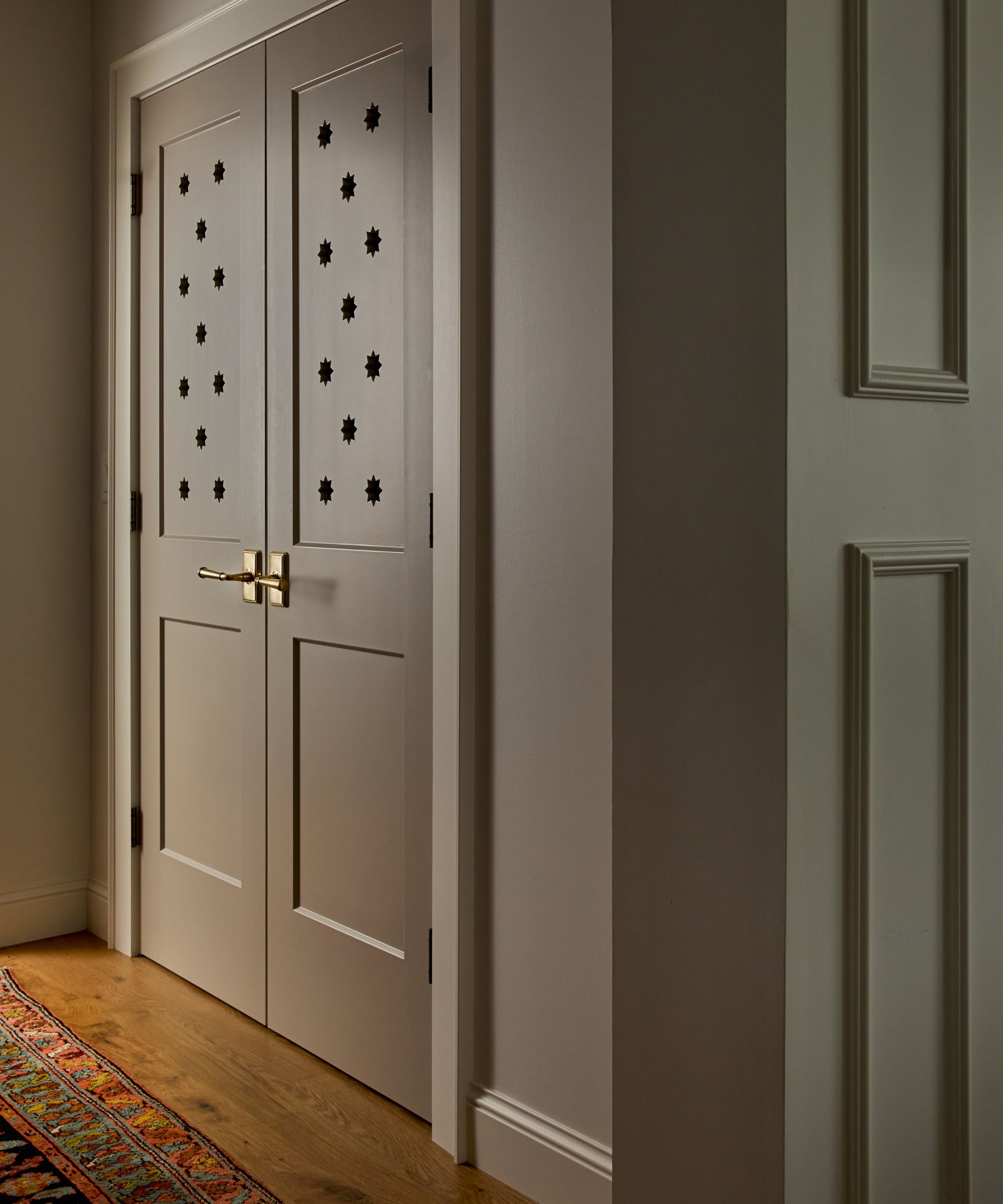 hallway doors painted a warm beige tone that lead to the pantry with brass hardware and star shaped cut out detailing on the door panel