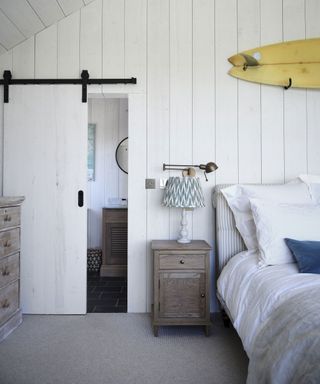 Neutral bedroom with cladding and surfboard in Cornish coastal newbuild