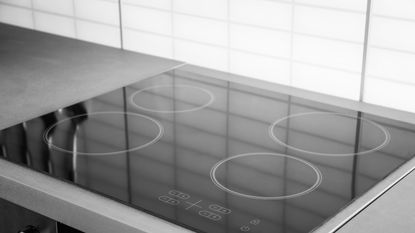 An image of a black glass stove top with a white tiled wall behind it and gray countertops next to it