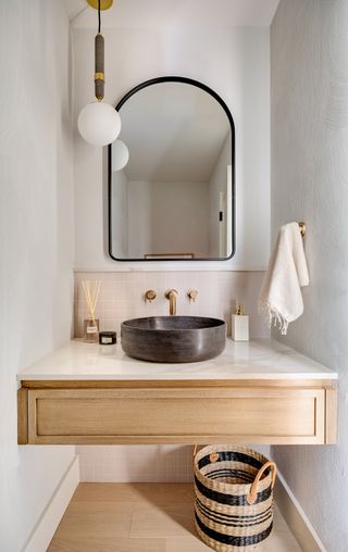 white small powder room with built in wall mounted vanity with drawer, stone sink, small tile backsplash, black mirror, globe pendant light, basket