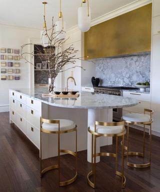 A gold and white kitchen with three bar stools