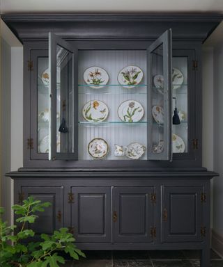 A black china cabinet with plates displayed inside