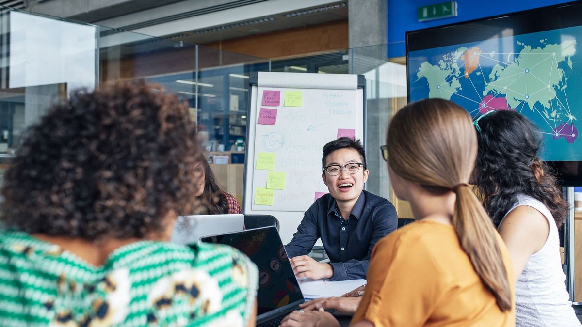 A diverse boardroom full of tech workers having a meeting, with a world map in the background