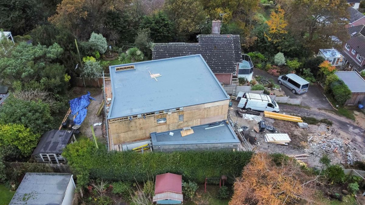 A large grey flat roofed self build with block walls surrounded by debris 