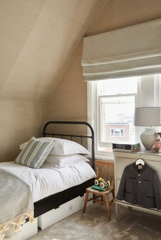 neutral boy's bedroom with ochre textured wallpaper, cream Roman blind, black iron bed