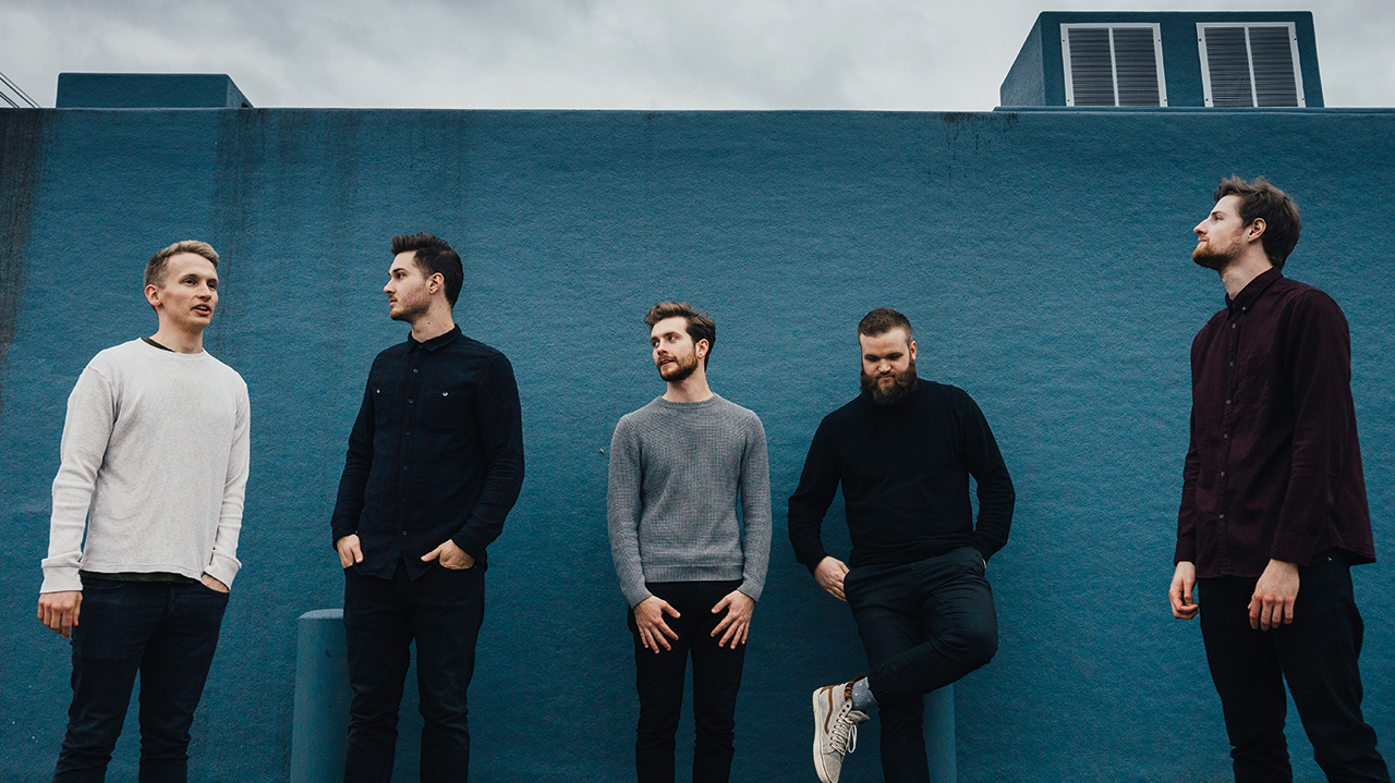 A press shot of Forevermore stood outside a blue building with a grey cloudy sky behind them