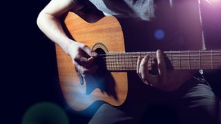 Musician playing acoustic guitar on dark background