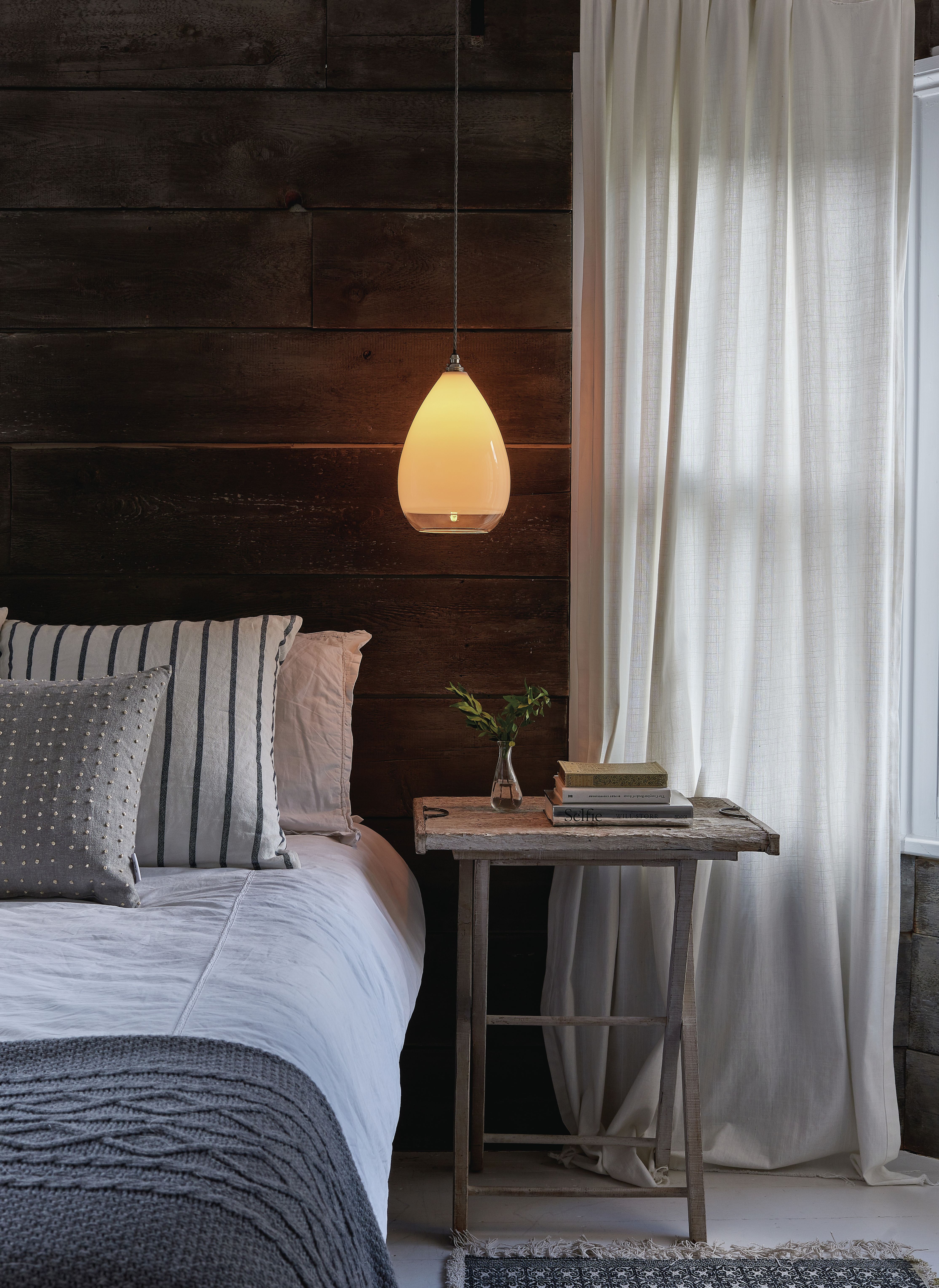 rustic style bedroom with wooden wall, linen curtain, pendant light above bedside, textured bedding, rug