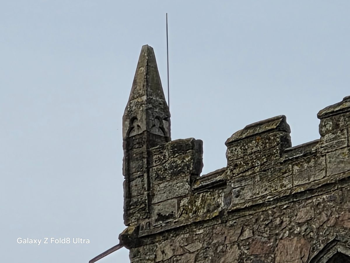 Heavily zoomed view of a pointed stone corner pinnacle and crenellations on a church tower.