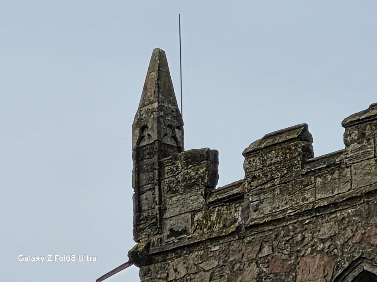 Heavily zoomed view of a pointed stone corner pinnacle and crenellations on a church tower.