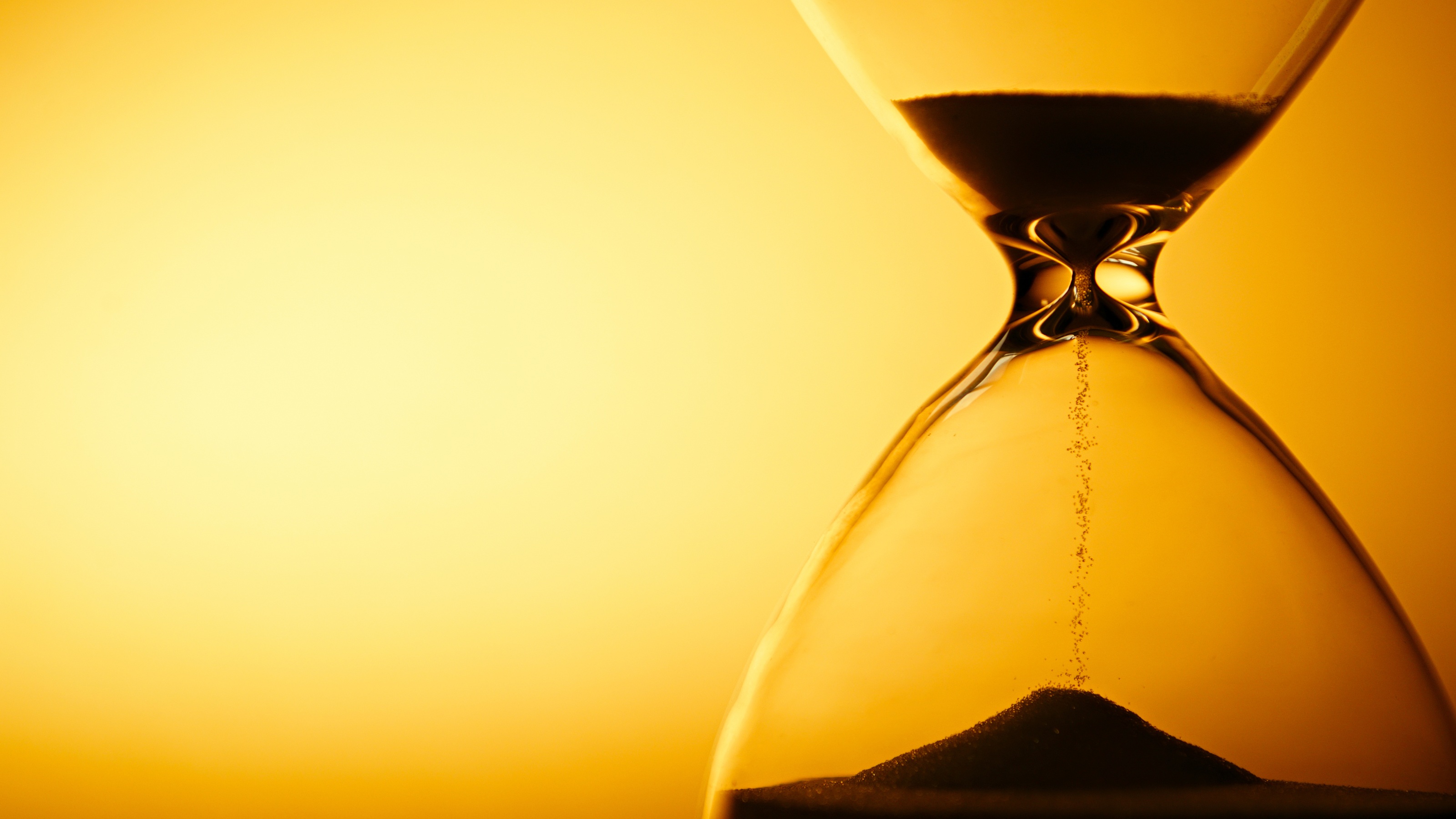 An hourglass with the sand almost done filtering into the bottom, against a yellow background.