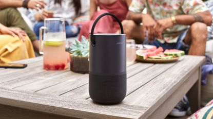 best outdoor speaker Bose Portable in black sitting on wooden garden table beside group eating and drinking