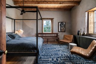 Blue rig with white pattern, black fourposter bed, brown leather chairs and wooden ceiling