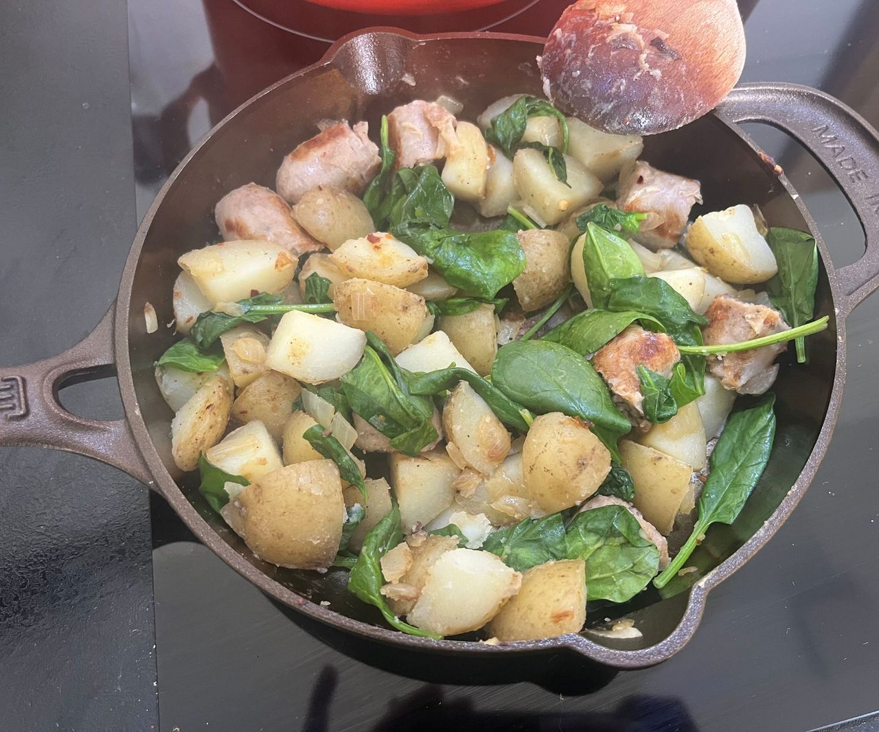 A small bronze colored cast-iron skillet with a sausages, potatoes, and spinach inside.