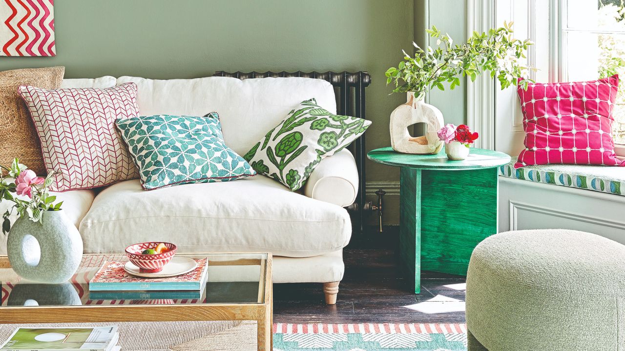 A sage green-painted living room with a cream sofa, a green stool and a green side table