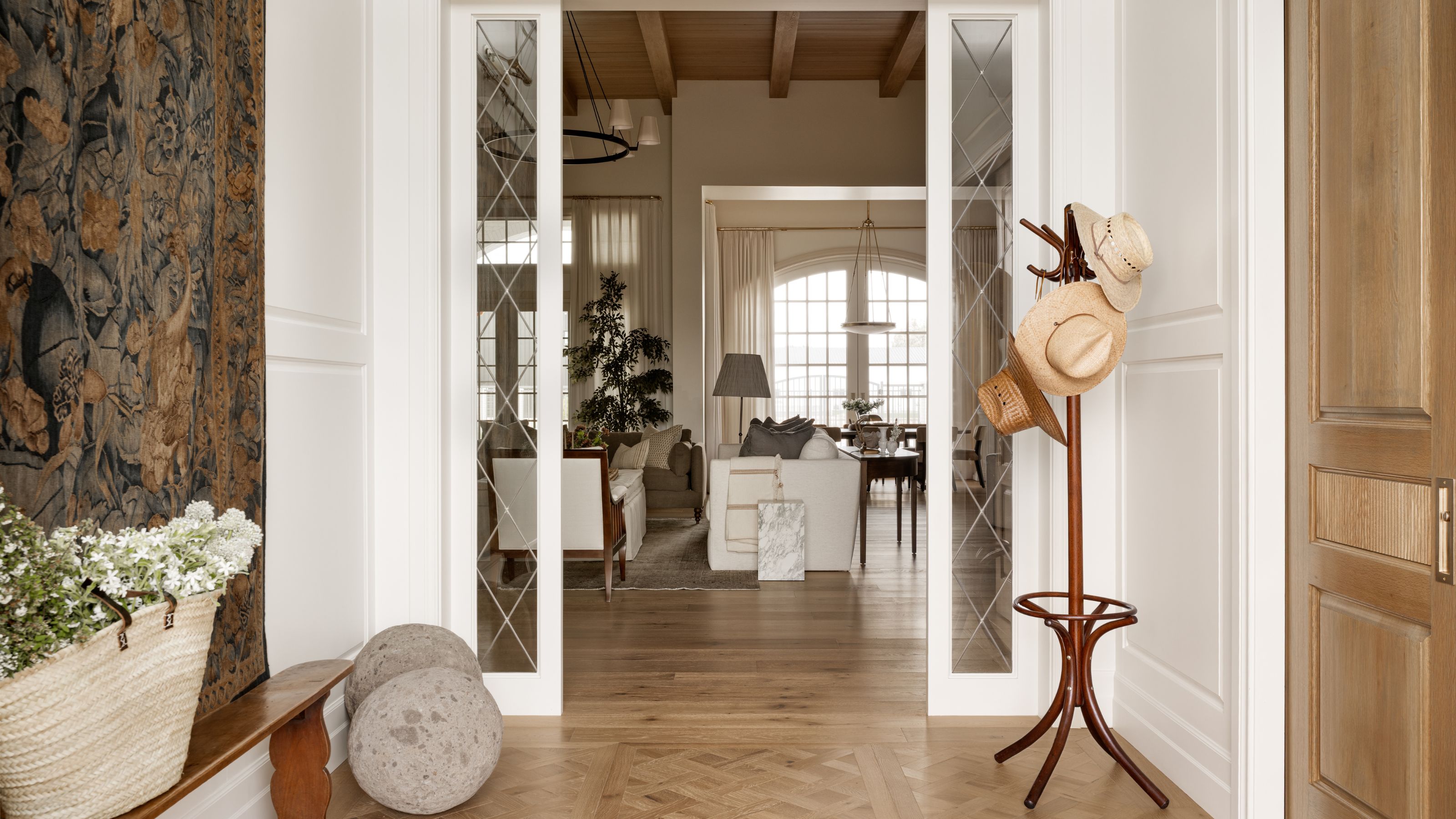 a layered entryway with leaded glass wall dividers, a hanging tapestry, parquet floor and a view through to the open living dining and kitchen area