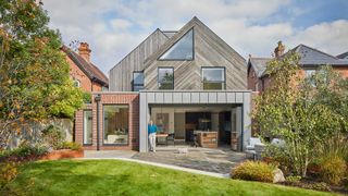 Homeowner standing in front of fully open glass bifold doors at the rear of a contemporary self-build home