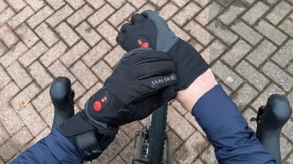 A rider putting a pair of SealSkinz Upwell heated cycling gloves on with the handlebars and bricked drive in the background