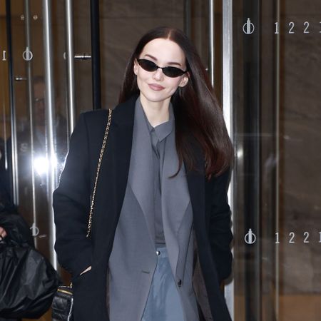 Dove Cameron wearing a black coat, grey top, gray pants, and black heels