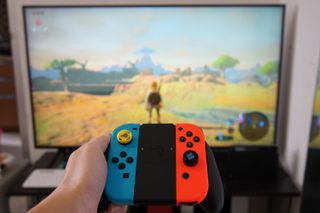 The best Nintendo Switch accessories: a hand holding a Nintendo Switch Joy-Con infront of a television screen