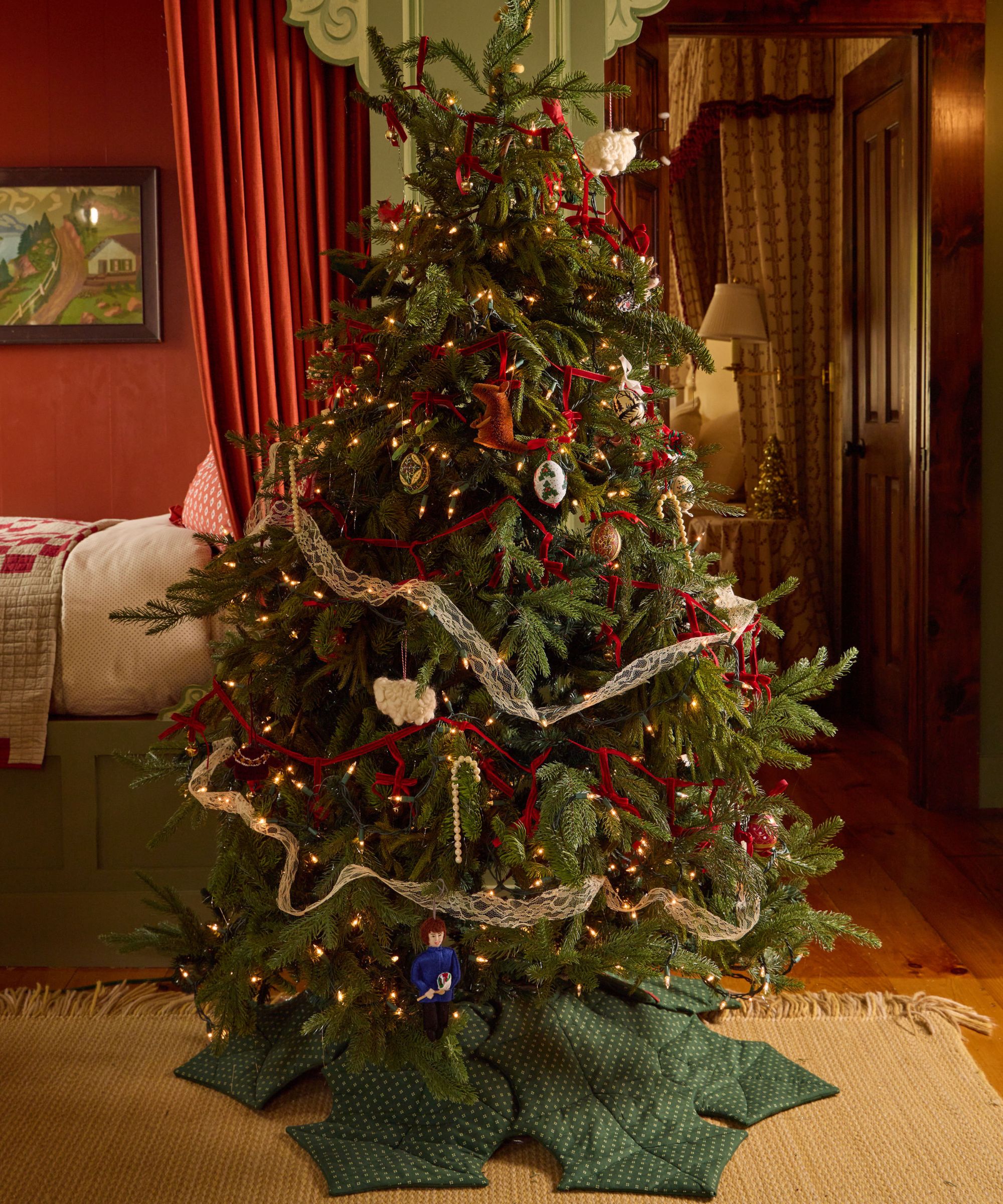 a bedroom at the six bells inn dressed for Christmas with a large christmas tree wrapped in lace and red ribbon garlands with egg baubles and felt ornaments