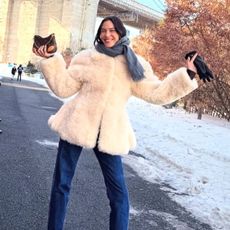 Alexa wears an ivory fur coat, blue jeans, and a gray scarf.